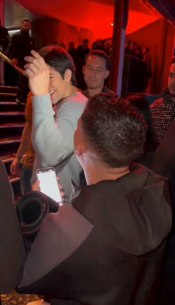 The man in the grey sweater raises a hand as the crowd films with phones